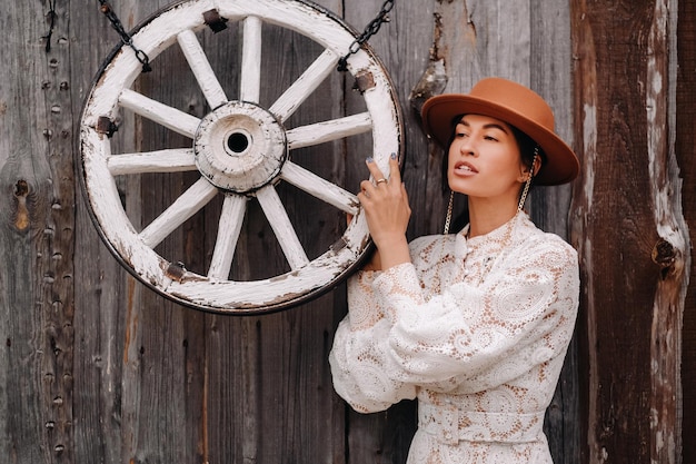 A female reenactor dressed in colonial attire is demonstrating the use of a spinning wheel. A small group of onlookers watches attentively as she spins yarn. The scene is set outdoors in a recreated colonial village.