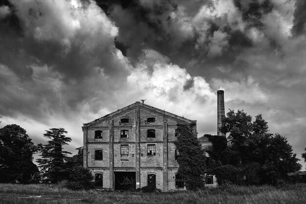 A black and white photograph of an old, abandoned factory building in a ghost town. The factory is large and imposing, with broken windows and overgrown vegetation. The image conveys a sense of industrial decline and the loss of economic opportunity.