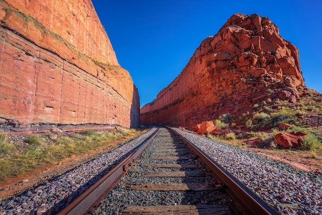 A wide, panoramic shot of the California Zephyr train traveling through the red rock canyons of Utah. The train is snaking along the tracks, and the landscape is bathed in golden sunlight.